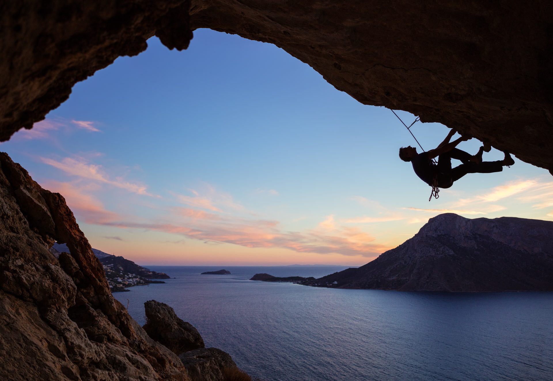 male-climber-climbing-along-roof-in-cave-at-sunset-e1695696702704.jpg