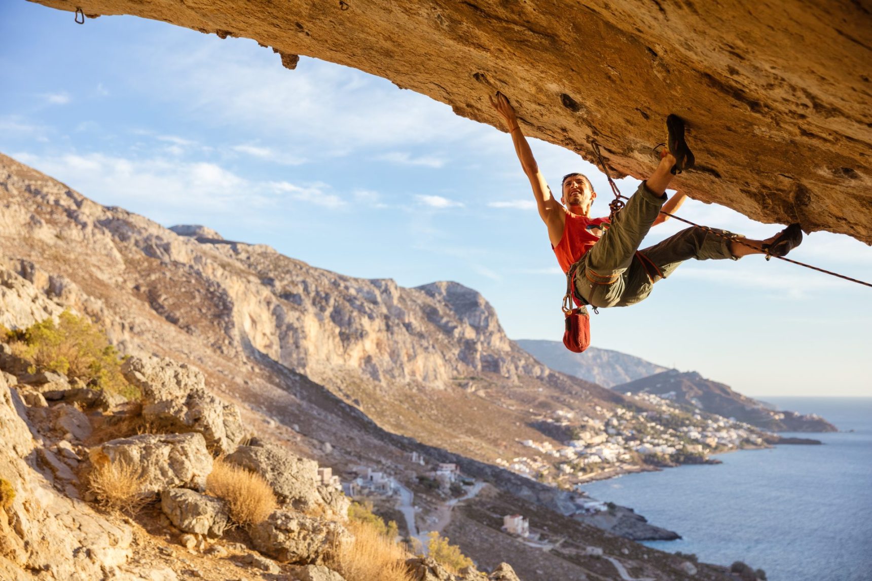 male-climber-on-overhanging-rock-against-beautiful-view-of-coast-below-e1695732106309.jpg