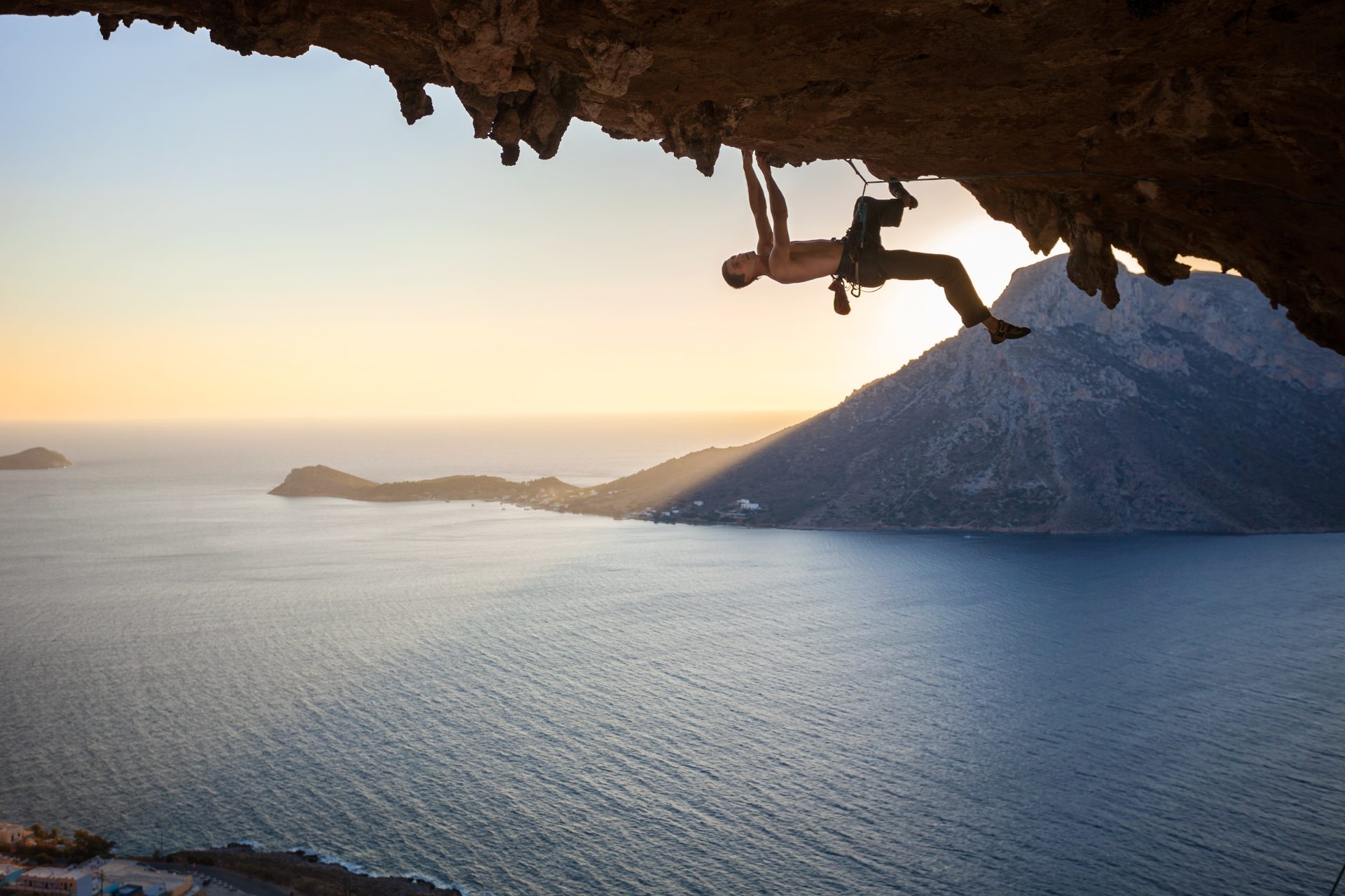 male-rock-climber-climbing-along-a-roof-in-a-cave-at-sunset-e1695696672830.jpg